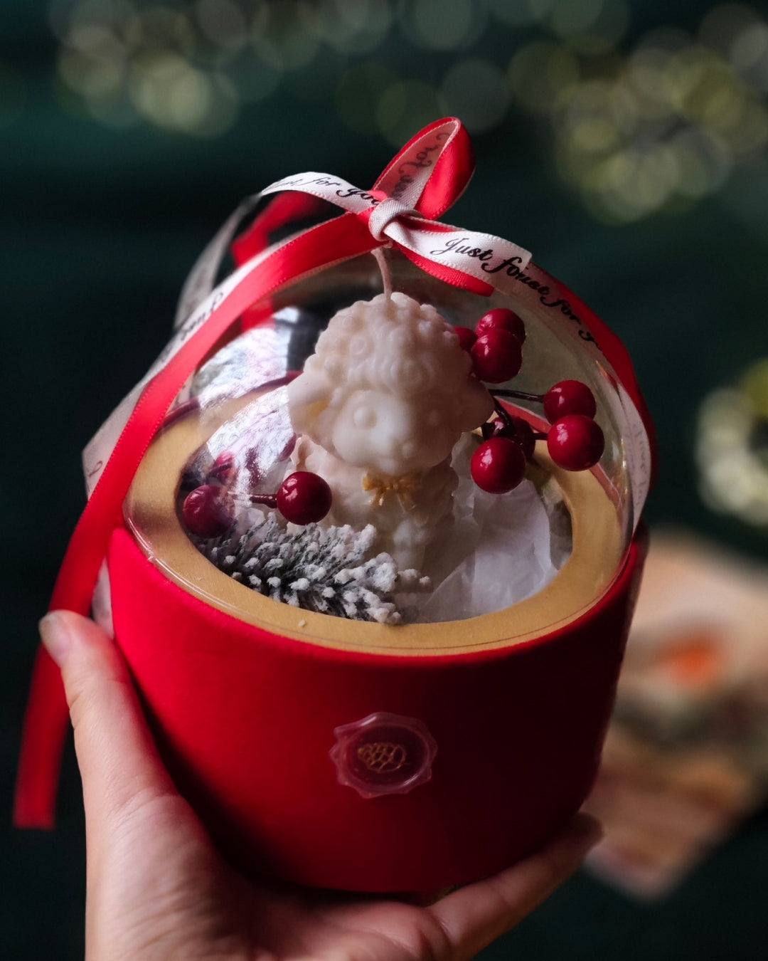 Rokā turēta svece Ziemas Brīnums Kupolā ar baltu figūriņu, sarkanām ogām un apsarmotu čiekuru zem kupola